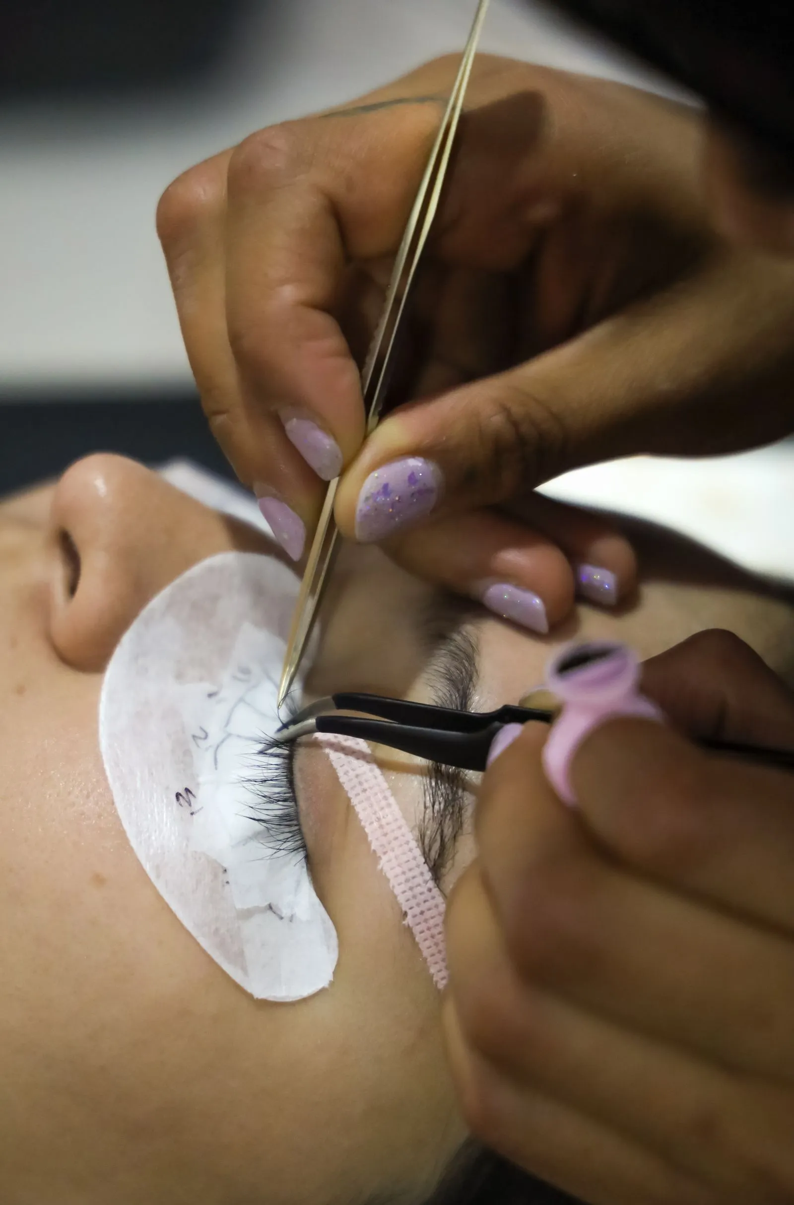 Especialista aplicando extensiones de pestañas con pinzas, vista de cerca.